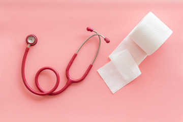 Toilet paper roll and stethoscope for proctology diseases concept on pink background top view
