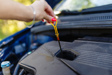 The female hand holds the dipstick oil level in the engine. Close-Up Of Woman Checking Car Engine Oil Level On Dipstick. Engine oil level testing