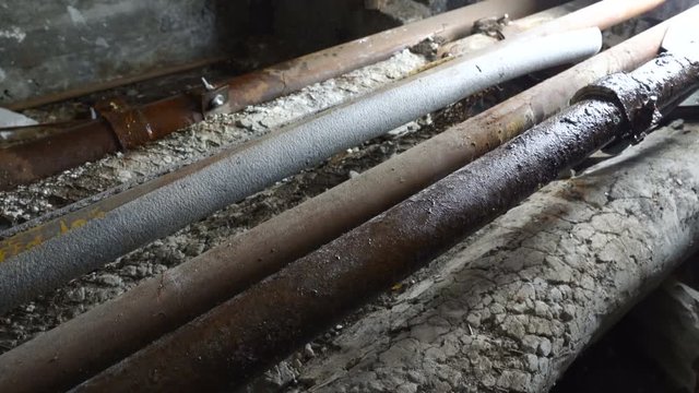 Water leaking from rusty plumbing pipes in basement of old house. Water drops splashing on iron pipe repair clamps. Dolly shot.