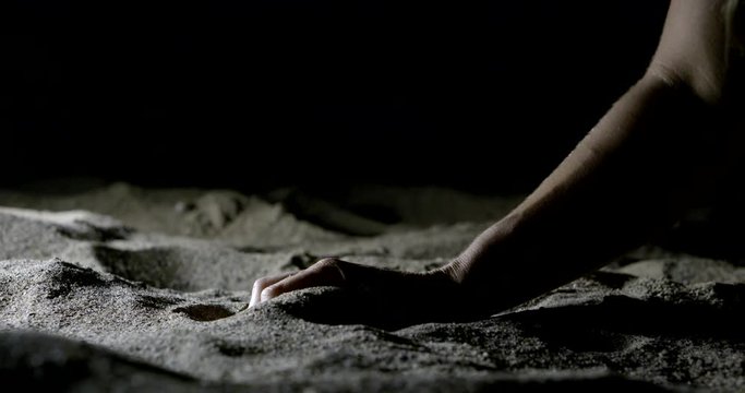 woman is taking sand by hand on beach in darkness, detail view of her palm