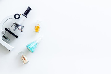 Laboratory desk with pills in test tube and microscope on white background top view space for text