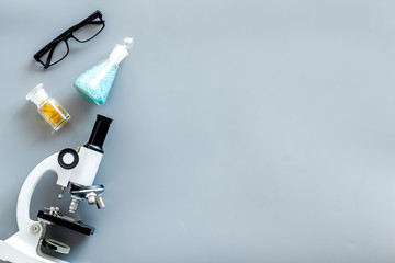 Laboratory desk with glasses, pills in test tube and microscope on gray background top view space for text