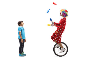 Boy watching a clown juggling and riding a unicycle