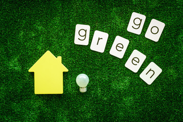 Go green copy and house with bulb on green texture background top view