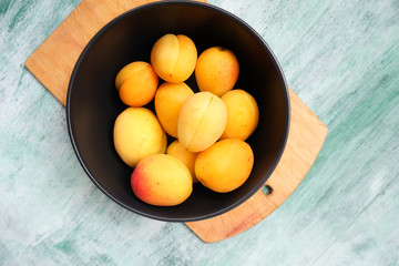 Fresh fruits on green wooden background. Sweet summer apricots in bowl. Top view.