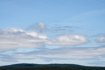 Nature background of blue sky and white puffy clouds, evergreen tree covered hill tops at the bottom, San Juan Islands