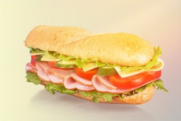 Long baguette sandwich with lettuce, vegetables, ham, and cheese on white background