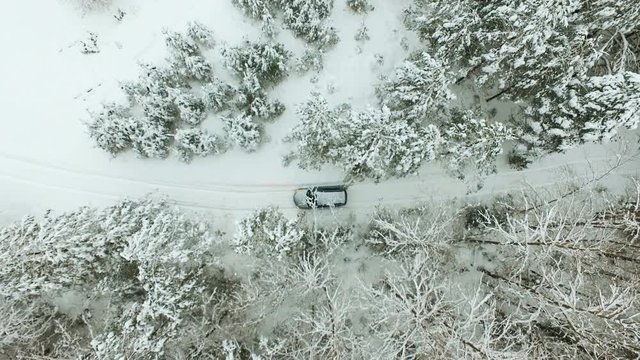 Aerial view of car driving on winter country road through snow covered forest.