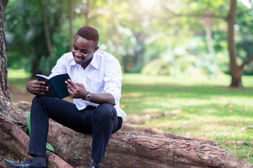 African man reading a book in the park.