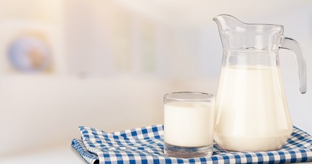A glass of milk and a milk jug on plaid tablecloth