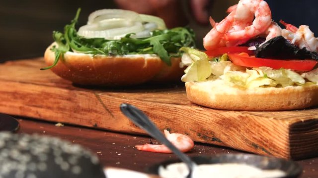 Close-up of small bowl with shrimps and male chef in blue apron taking a few shrimps and adding them in a hamburger. Stock footage. Preparing of delicious hamburgers
