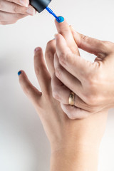 A mother paints her young girl's hands with blue and pink nailpolish, viewed against an isolated white background