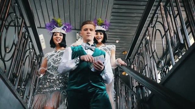 Retro theme party - A young man walking downstairs accompanied by two women in brilliant clothes - scattering his money