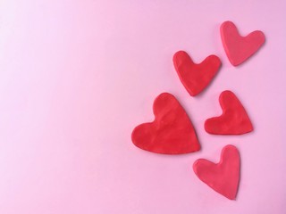 Many red heart made from plasticine clay on pink background, cute shaped dough 