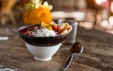 smoothie bowl in a coconut shell plate with with strawberries, chia seeds, banana, granola, flower on wooden background