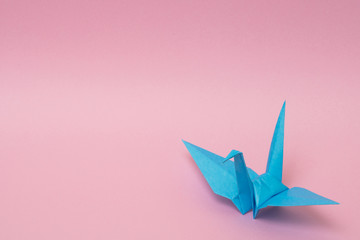 light blue origami paper crane on pink background