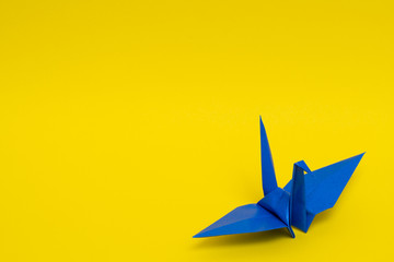 blue origami paper crane on yellow background