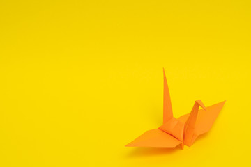 orange origami paper crane on yellow background