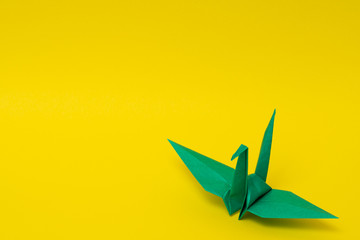 green origami paper crane on yellow background