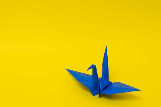 blue origami paper crane on yellow background