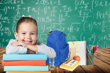 Little cute girl with books near green blackboard