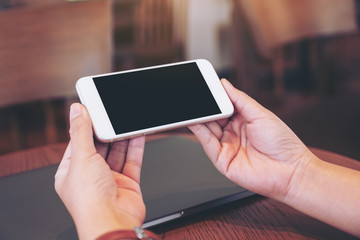 Mockup image of hands holding white mobile phone with blank desktop screen with laptop computer on the table