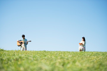 草原でギターを弾く男性と本を読む女性