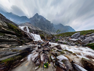 Fototapeta na wymiar Mountain waterfall stream in misty rainy weather in the valley flowers