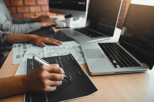 Two software developers are using computers to work together with their partner at the office desk.