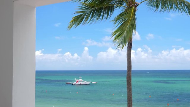 View from balcony resort on caribbean beach with coconut palm trees and boat floating in turquoise sea. Travel destinations. Summer vacation