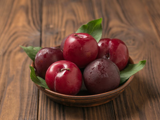 Clay bowl with ripe fresh plums on a wooden table.