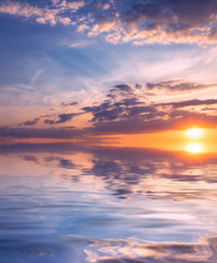 Heavenly sunset with the rays of the sun in the blue sky over the quiet, calm sea.