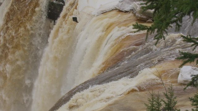 Magestic shot of Alexandra Falls in the Northwest Territories flowing though ice druing spring breakup in slow motion. Trees in the foreground.