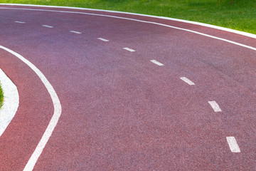 Red synthetic treadmill or cycle track with white markings, turns to the left
