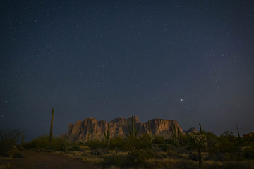 The desert wilderness east of Phoenix, Arizona photographed under clear starry desert skies that seem to glow with color. Desert plants and Saguaro cactus grow around the Superstition mountains 