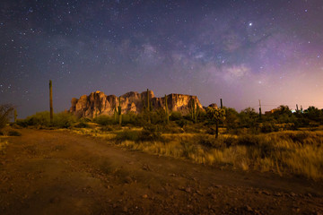 Fototapeta premium The iconic Superstition Mountains east of Phoenix, Arizona glow under the desert night sky and the epic Milky Way Our world under our universe in star filled dark skies is natural beauty