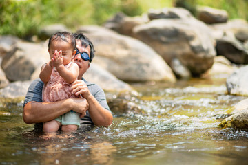 Asian man wearing goggles holding his baby girl in water
