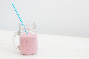 fresh cold pink smoothie on white background with blue straw 