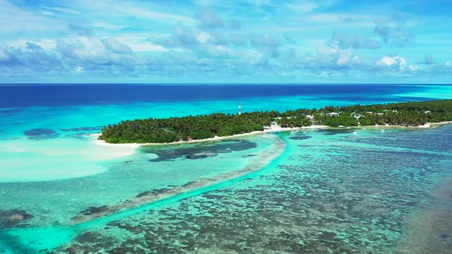 Aerial view of a reef in the turquoise water in front of a tropical island with a forest and village on it. In Thailand. A cloudy blue sky.