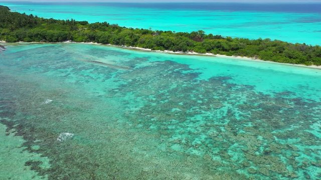 Flight towards an exotic island with trees on it. Shallow water with reefs in front of it. Dolly in, Indonesia