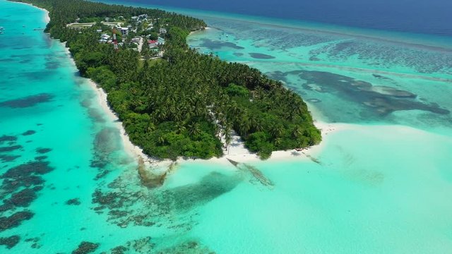 Aerial view of a tropical island with a forest and houses on it. In the turquoise sea of the Gulf of Thailand. tilt up.