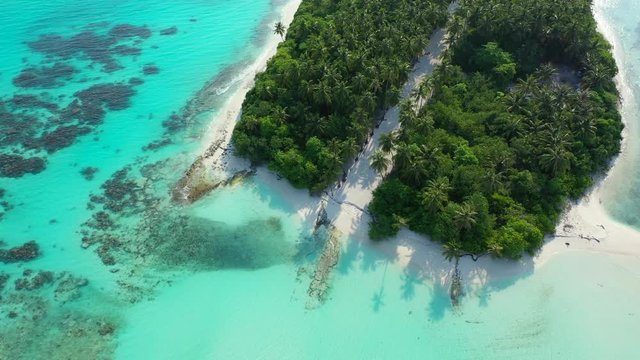 Looking down during a slow flyover a exotic island with a forest and sandy paths on it. Located in teh turquoise sea of Indonesia. Dolly in