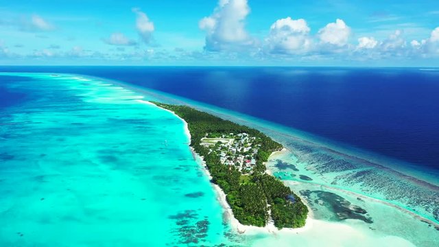 Aerial view of a tropical island with trees, houses on it.  In the turquoise Gulf of Thailand, which turns blue in the distance. A blue sky with clouds in the background. dolly in