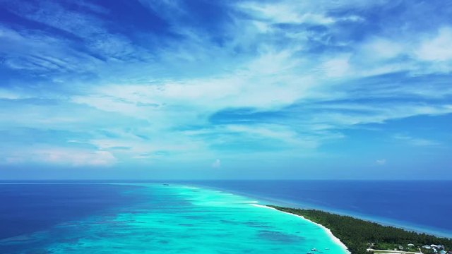 Aerial view from high above on a tropical island with palm trees and some buildings on it. Turquoise water of the Philippines under a blue sky with clouds. Pan left