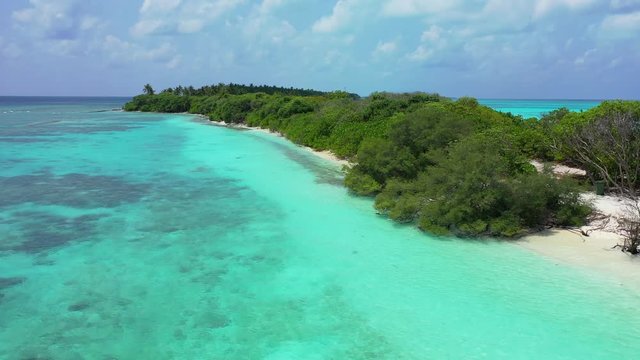 Flight towards and along a thin exotic island. Bushes on the island. Turquoise water in front of it. In Hawaii. Dolly in