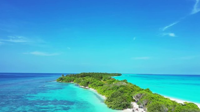 Flight over a tropical island in a circular movement. Turquoise water of the sea in Hawaii, a sandy beach and some bushes. A blue sky.