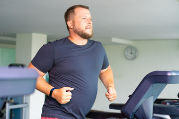 Fototapeta na wymiar chubby man walking on running track, warming up on gym treadmill.