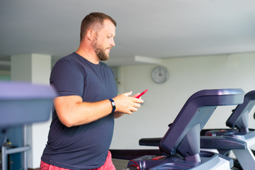 Fototapeta na wymiar chubby man walking on running track, warming up on gym treadmill. man with phone