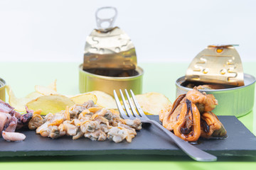 Tasty seafood, mussels served with cockles and poton on a black plate with cans of open seafood decorating the photo
