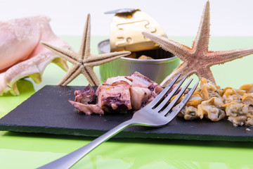 Fresh sliced poton, cockles served on a black stone board and a fork adorned with a couple of starfish.